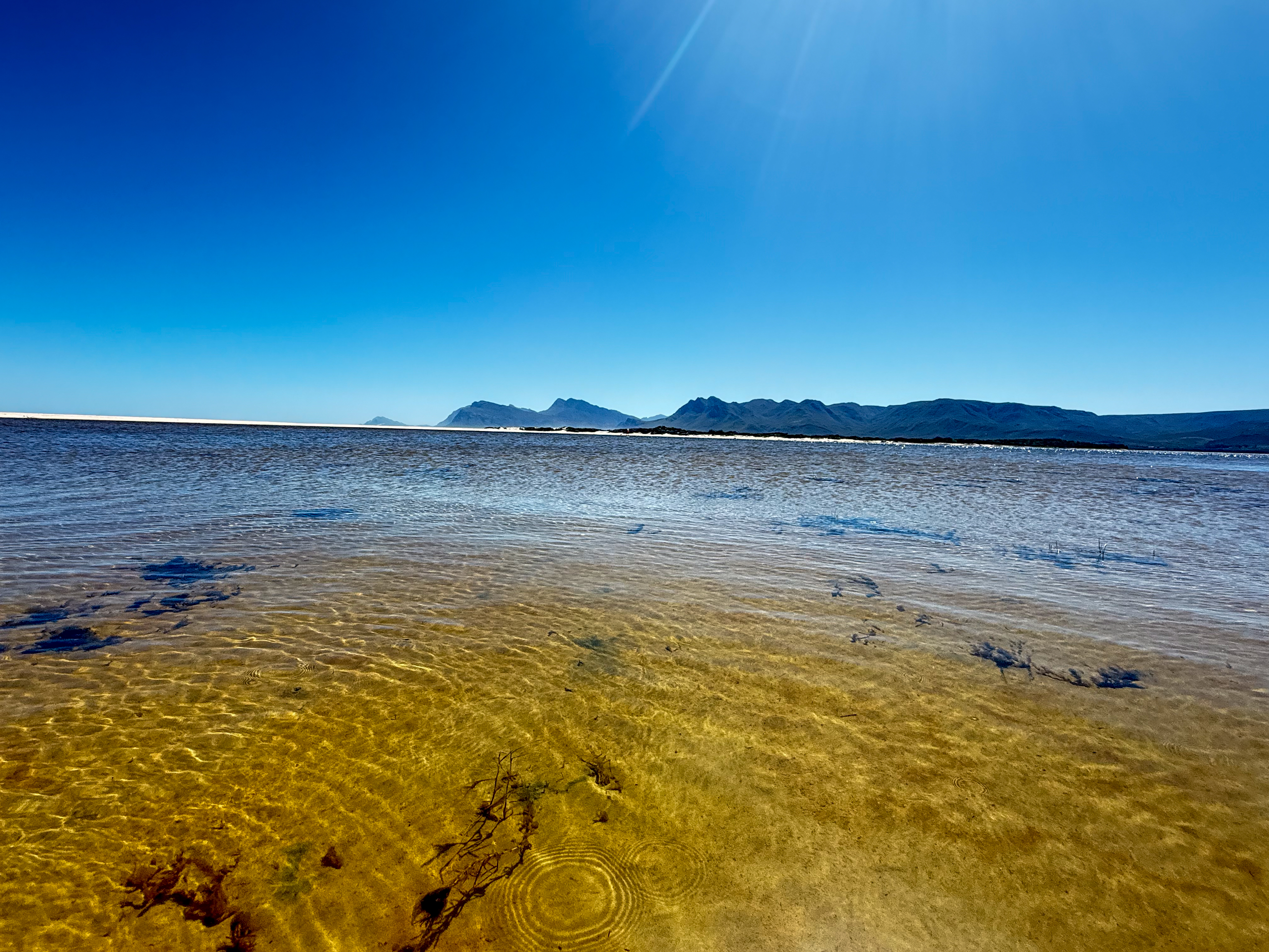 The Kleinrivier Lagoon with crystalline water and Overberg mountains on the horizon — the view that greets hikers returning to MBIZI lagoon house