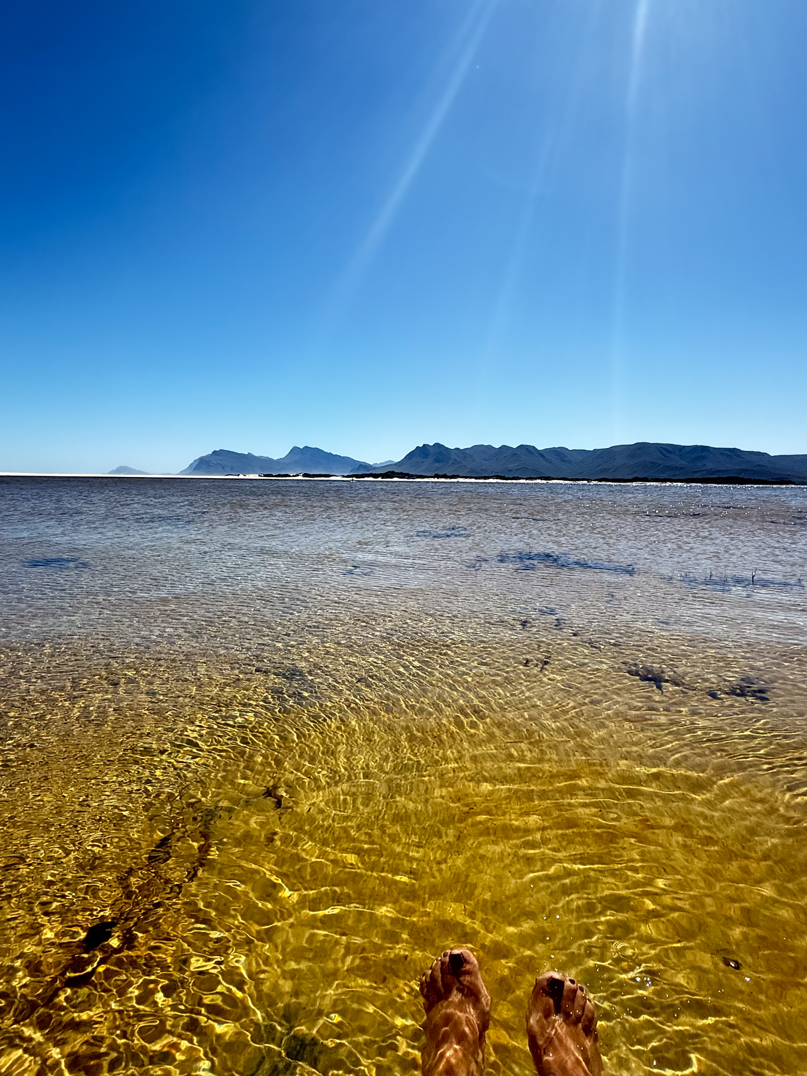 Feet in the warm clear water of the Kleinrivier Lagoon with Overberg mountains on the horizon — the reward after a day's hiking near Hermanus