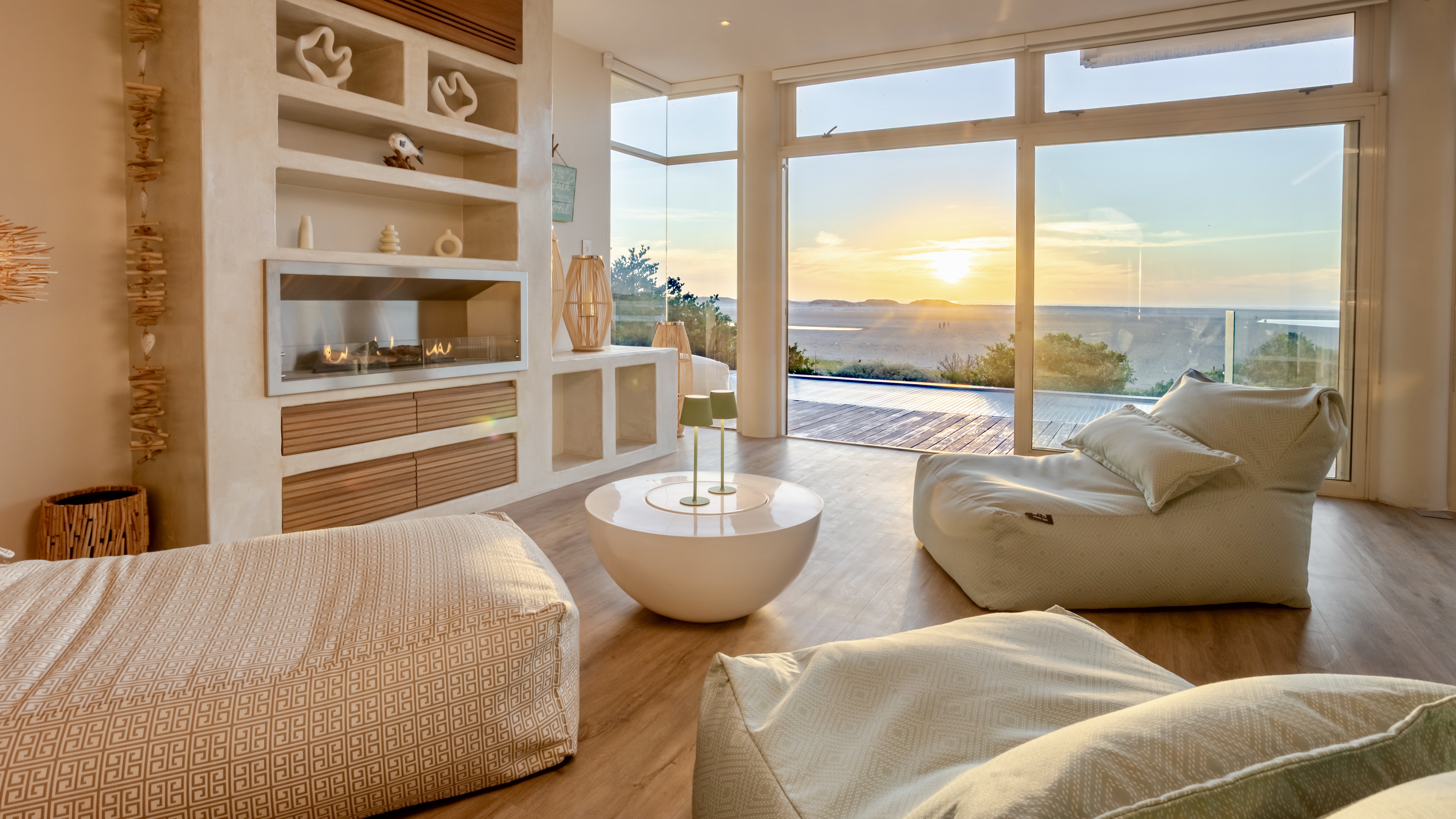 MBIZI lagoon house open-plan lounge with floor-to-ceiling windows, fireplace and sunset view over the Kleinrivier Lagoon